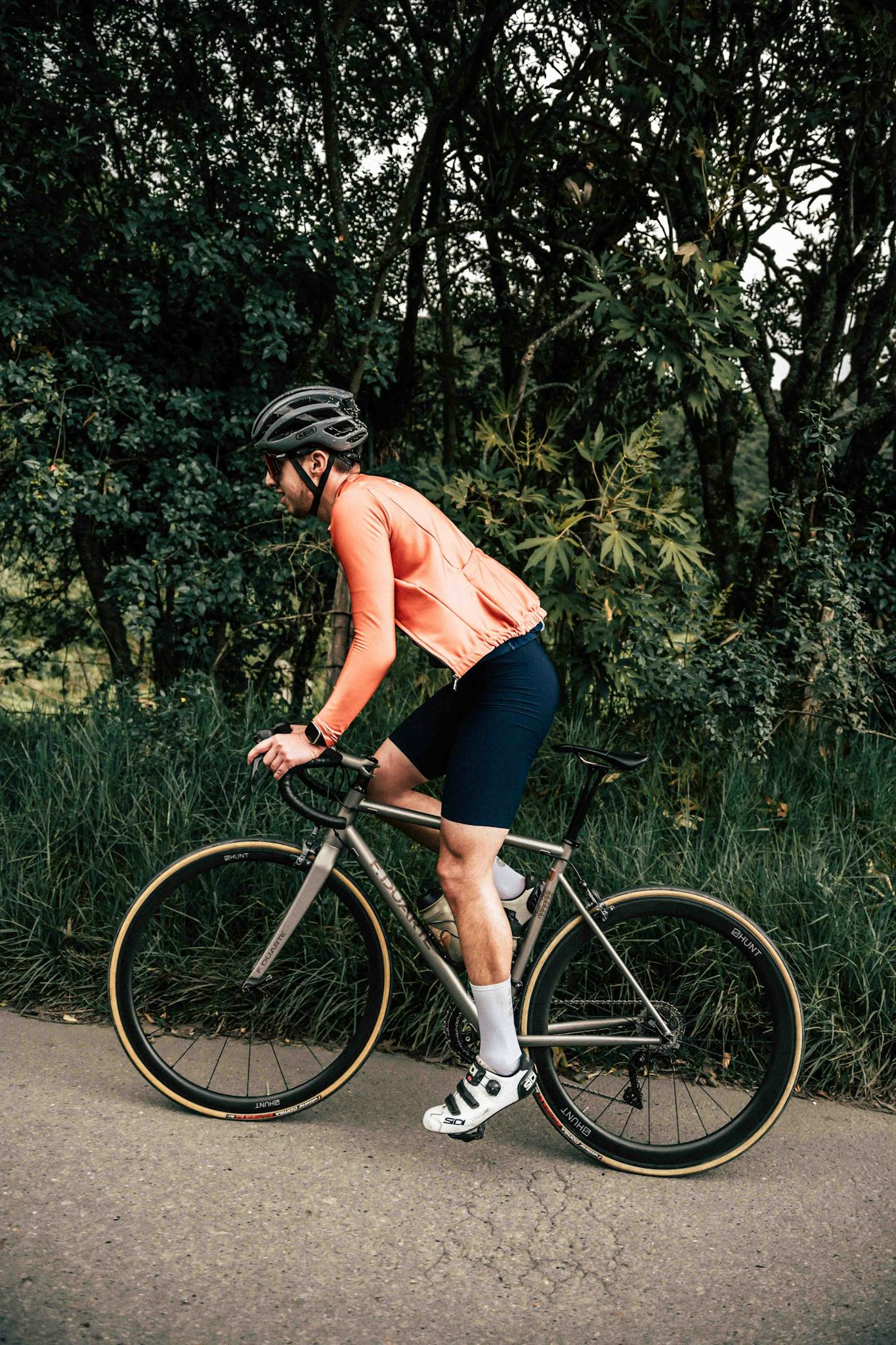 A man riding a bicycle on a road surrounded by lush greenery, wearing a helmet and sports attire.