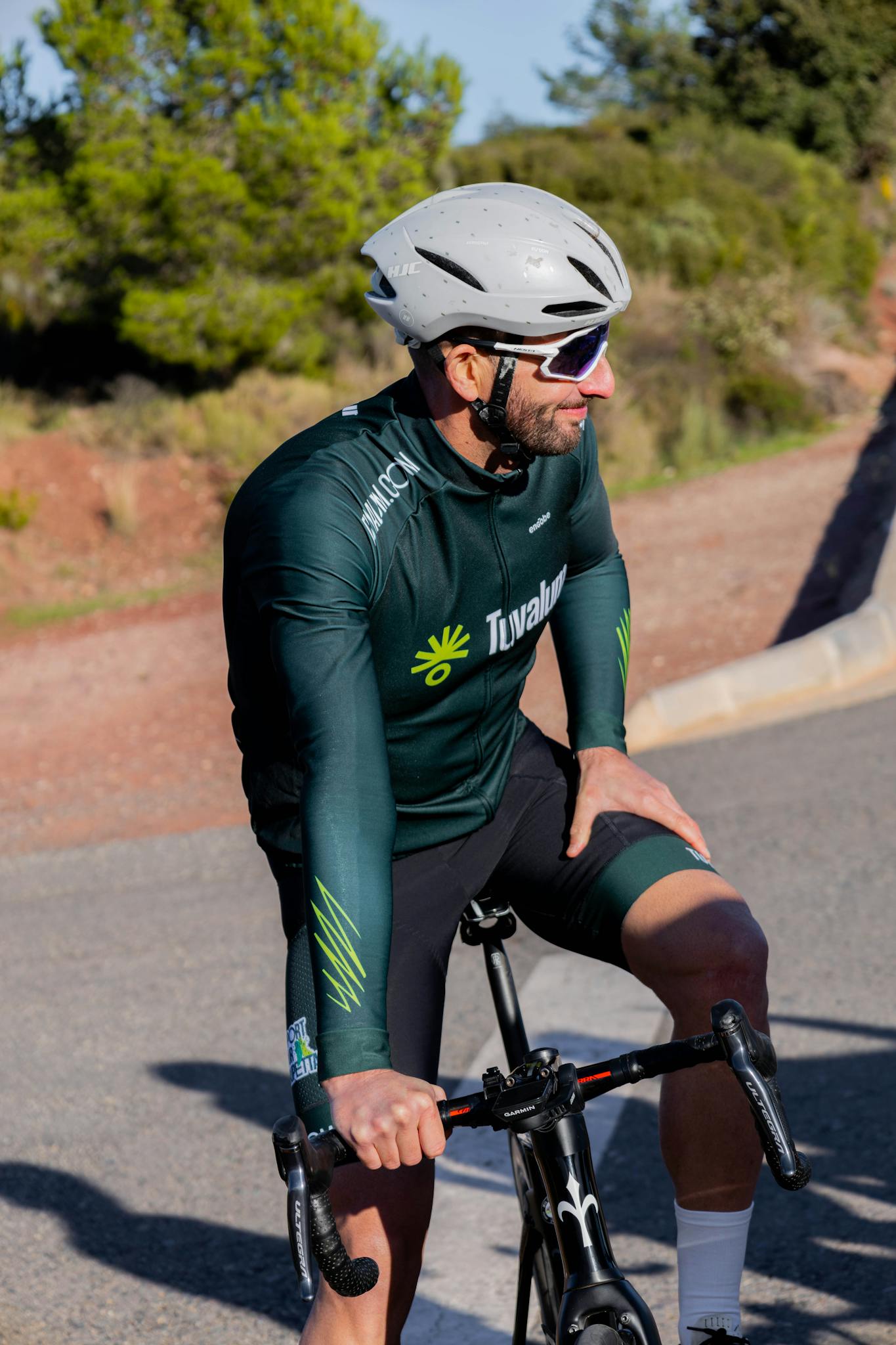 Male cyclist in green sportswear and helmet taking a break outdoors on a sunny day.
